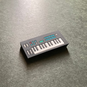 May include: A black toy keyboard with white keys and blue and red buttons. The keyboard has a blue and green display screen.