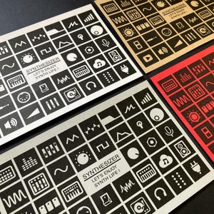 Puede incluir: Cuatro tarjetas con gráficos de sintetizador en blanco y negro. Cada tarjeta presenta una cuadrícula de iconos y el texto "SYNTHESIZER LET'S ENJOY SYNTH LIFE!". Las tarjetas están sobre una superficie negra, con una tarjeta roja y otra beige.