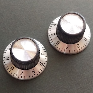 May include: Two silver and black knobs with numbers 4 through 9 printed around the edge. The knobs have a silver metal top and a black plastic base.