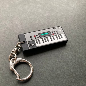 Può includere: Un portachiavi nero e argento a forma di sintetizzatore vintage con un anello portachiavi argentato.