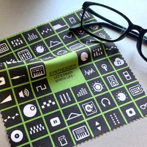 Könnte beinhalten: Ein Mikrofasertuch mit einem schwarz-grünen Gittermuster mit weißen Synthesizer-Symbolen. Auf dem Tuch steht der Text "SYNTHESIZER LET'S ENJOY SYNTH LIFE!" und daneben liegt eine Brille mit schwarzem Rahmen.