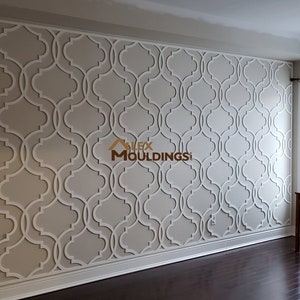 Puede incluir: Una pared blanca con un patrón decorativo de arcos entrelazados. El patrón está hecho de molduras blancas sobre una pared beige claro. La pared está en una habitación con suelo de madera y una ventana con cortinas blancas.