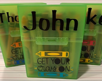 Op de afbeelding: Drie groene plastic doosjes voor kleurpotloden met de tekst "Get Your Cray On" en een kleurpotlood-illustratie. De doosjes zijn gelabeld met "John", "Tha" en "Ke".