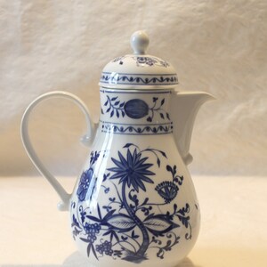 Może przedstawiać: Biały porcelanowy dzbanek do kawy z niebiesko-białym wzorem kwiatowym. Dzbanek ma pokrywkę i uchwyt.