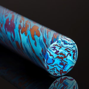 Puede incluir: Primer plano de una varilla de metal con patrón azul, morado y naranja. La varilla es cilíndrica y tiene un acabado liso y pulido.