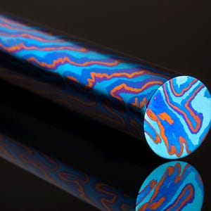 Può includere: Primo piano di un'asta di metallo con motivo blu e arancione. L'asta è rotonda e ha una finitura liscia e lucida.