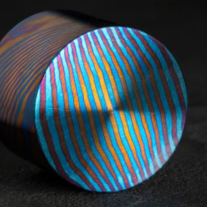 Puede incluir: Primer plano de un objeto cilíndrico con un acabado iridiscente azul, naranja y morado. El objeto tiene un patrón de líneas en espiral.