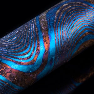 Puede incluir: Primer plano de un bolígrafo de metal azul y marrón con un patrón ondulado. El bolígrafo tiene un brillo metálico y una superficie texturizada.