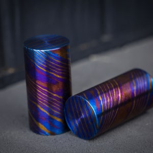 Puede incluir: Dos objetos metálicos cilíndricos con un patrón de remolino azul, morado y dorado.