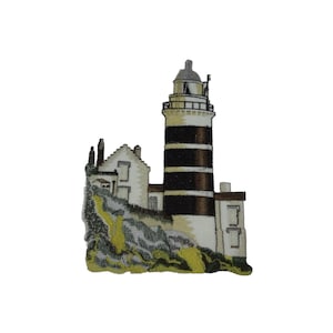 Puede incluir: Parche bordado de un faro blanco con rayas negras en un acantilado rocoso. El faro tiene un pequeño edificio blanco adjunto.