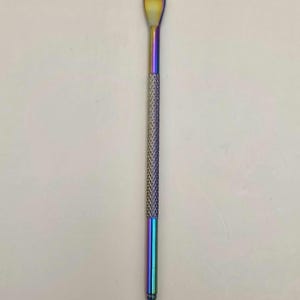 May include: A multi-colored metal tool with a spoon-shaped end and a pointed tip. The tool has a textured, diamond-patterned grip in the middle. The color transitions from gold to blue and purple.