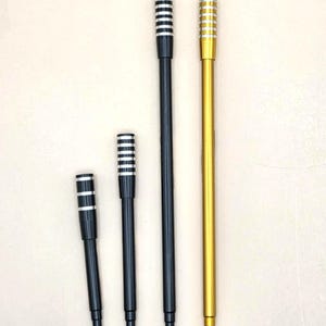 May include: Four slender, elongated cigarette holders arranged vertically. Three holders feature black shafts with silver-toned, ribbed mouthpieces. The fourth holder on the far right has a gold-toned shaft with a matching gold-toned, ribbed mouthpiece.
