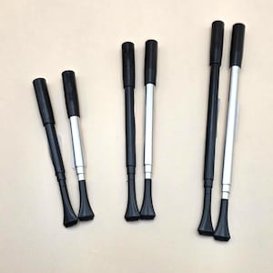 May include: Three pairs of telescopic cigarette holders in varying lengths. Each holder features a black mouthpiece, a black cylindrical handle, and a silver-toned extendable metal shaft that tapers to a flared end. The items are arranged vertically.