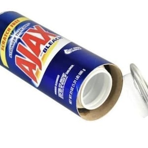 May include: A blue and white Ajax Bleach container with the lid partially removed, revealing a white interior. The label reads "Ajax Bleach" and "Scratch Free". The container is 595 g.