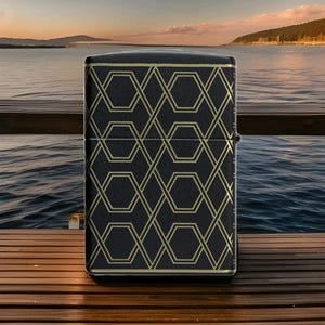 Puede incluir: Encendedor negro con un patr&oacute;n geom&eacute;trico dorado. El dise&ntilde;o presenta l&iacute;neas que se cruzan y formas hexagonales. El encendedor se encuentra sobre un fondo esc&eacute;nico de agua y un muelle de madera.
