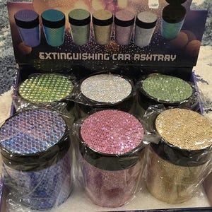 Puede incluir: Exhibición de ceniceros para coche en varios colores, incluyendo azul, verde, rosa y dorado. Cada cenicero tiene un acabado brillante y una tapa negra. El embalaje dice "EXTINGUISHING CAR ASHTRAY".