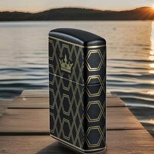 Puede incluir: Encendedor negro con un patr&oacute;n geom&eacute;trico dorado y un emblema de corona. El encendedor est&aacute; sobre un muelle de madera, con un lago y una puesta de sol de fondo. El encendedor tiene forma rectangular.