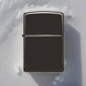 May include: A shiny, black metal lighter with a rectangular shape. The lighter has a hinged lid and a silver-colored border. The background is a snowy, white surface.
