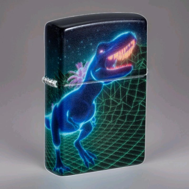 Puede incluir: Encendedor negro con un dise&ntilde;o de Tyrannosaurus Rex azul ne&oacute;n. El dinosaurio est&aacute; sobre un fondo estrellado y una cuadr&iacute;cula verde. El encendedor tiene una bisagra plateada.
