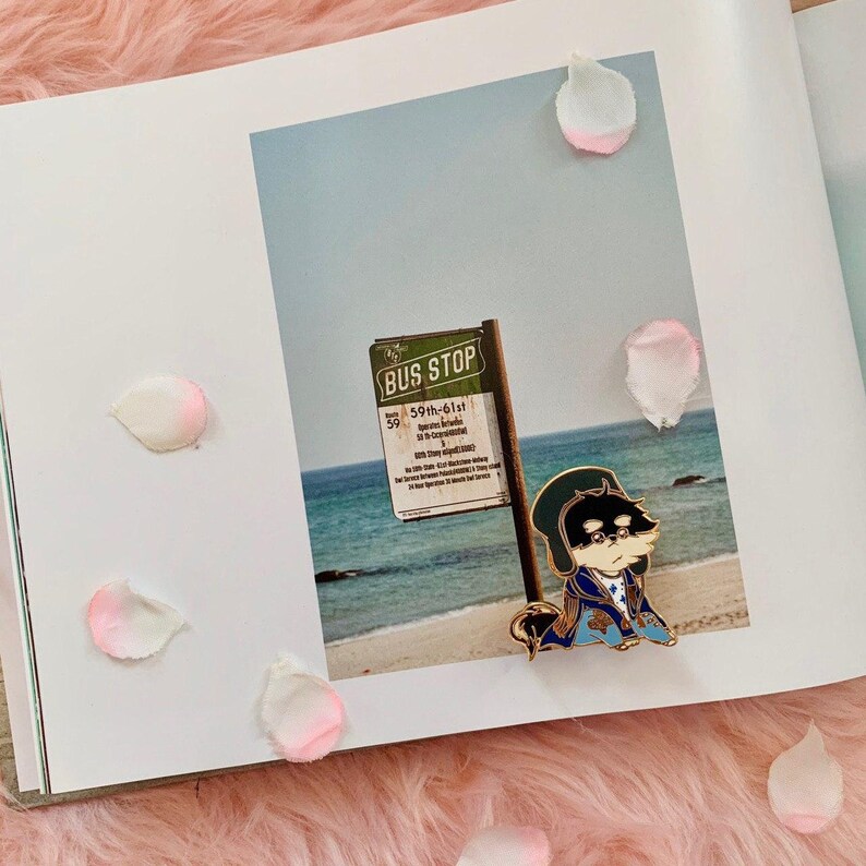 Puede incluir: Un pin de esmalte dorado con un personaje de dibujos animados que lleva una chaqueta azul y un sombrero negro. El personaje est&aacute; de pie frente a un cartel que dice "Bus Stop 59th-61st".