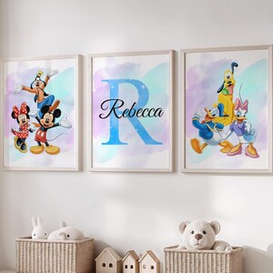 Könnte beinhalten: Drei gerahmte Drucke mit Disney-Figuren. Einer zeigt Micky und Minnie Maus mit Goofy. Ein anderer hat einen großen blauen Buchstaben "R" mit dem Namen "Rebecca". Der dritte Druck zeigt Donald Duck, Daisy Duck und Pluto. Die Drucke haben einen Aquarellhintergrund.