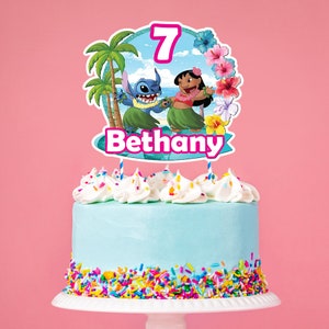 Puede incluir: Una tarta de cumplea&ntilde;os con glaseado azul, chispas de colores y remolinos de glaseado blanco. Un adorno para tarta presenta el n&uacute;mero 7, el nombre "Bethany" y los personajes de dibujos animados Stitch y Lilo en un entorno tropical.