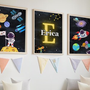 Könnte beinhalten: Drei gerahmte Wandbilder mit Weltraummotiven auf dunklem Hintergrund. Das linke Bild zeigt einen Astronauten auf einem Planeten mit Flagge, Satelliten und Planeten. Das mittlere Bild zeigt einen großen gelben Buchstaben E und den Namen Erica. Das rechte Bild zeigt eine Rakete, eine Galaxie und Planeten.