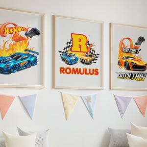Peut inclure: Trois affiches encadrées représentant la marque Hot Wheels, des voitures de course et des flammes. L'affiche de gauche montre une voiture bleue, celle du centre affiche la lettre R et le nom ROMULUS, et celle de droite présente une voiture orange avec le texte YOU CAN'T CATCH THIS.
