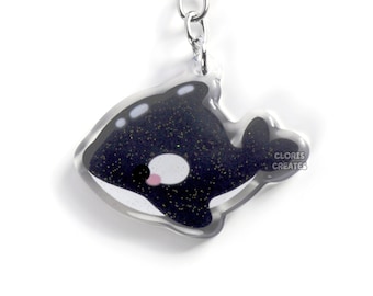 May include: A black and white orca keychain with glitter embedded in the black part of the orca. The keychain is made of clear acrylic and has a silver metal key ring.