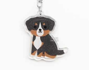 May include: A black, brown, and white Bernese Mountain Dog keychain with glitter accents. The keychain is made of clear acrylic and has a silver metal key ring.