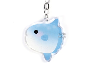 Peut inclure: Un porte-clés en forme de poisson-lune bleu et blanc en dessin animé avec un anneau de clé argenté. Le porte-clés est fait d'acrylique transparent et a une finition brillante. Le poisson a une expression mignonne et de dessin animé et est entouré d'une bordure blanche. Le texte "CLORIS CREATES" est imprimé sur la queue du poisson.