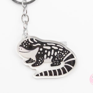 May include: Black and white lizard keyring with glitter accents. The keyring is made of clear acrylic and has a silver metal ring.