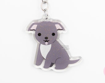 Puede incluir: Un llavero plateado con un dije de perro de dibujos animados morado y blanco. El dije tiene brillantina y el texto "CLOVER CREATES" está impreso en el dije.