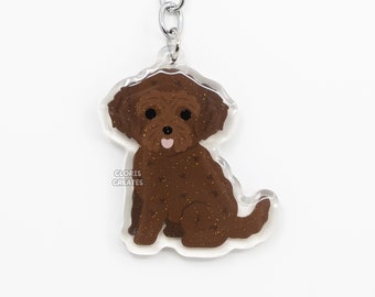 May include: Brown and white glitter poodle dog keychain with a silver key ring. The keychain is made of clear acrylic and features a cartoon illustration of a poodle dog.