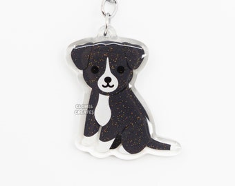 May include: Black and white dog keychain with glitter accents. The dog is sitting and has a silver chain attached to the top.