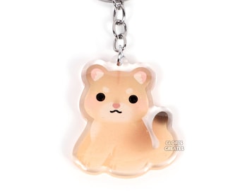 May include: A clear acrylic keychain featuring a light brown Shiba Inu dog design. The keychain has a silver metal ring and chain. The dog has black eyes and a small black mouth. The keychain has the text "GLORIS CREATES" on the bottom right.