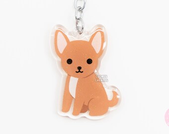 May include: A brown and white chihuahua keychain with glitter accents. The keychain is made of clear acrylic and has a silver metal chain and ring.