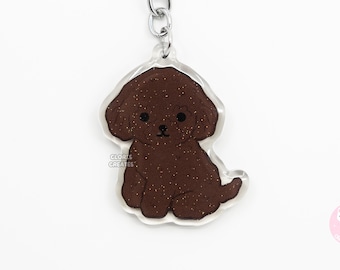 May include: A brown glitter poodle keychain with a silver key ring. The keychain is made of clear acrylic and features a cartoon-style poodle with a brown glitter finish.