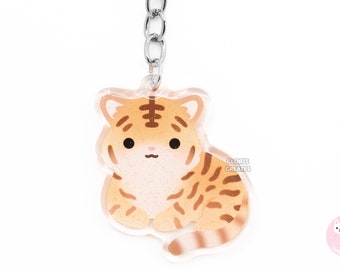 May include: A clear acrylic keychain featuring a cartoon tiger with orange and brown stripes. The keychain has a silver metal chain and ring. The tiger has a cute, friendly expression. The text "Cloris Creates" is visible on the right side.