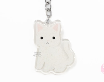 May include: White glitter cat keychain with a silver key ring and chain. The keychain features a white cat with pink ears and a white glitter background. The text "CLORIS CREATES" is printed on the keychain.