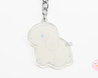 Puede incluir: Llavero de conejito blanco con purpurina y un ojo azul. El llavero está unido a un anillo y una cadena de metal plateado. El texto "CLORIS CREATES" está impreso en la esquina inferior derecha del llavero.