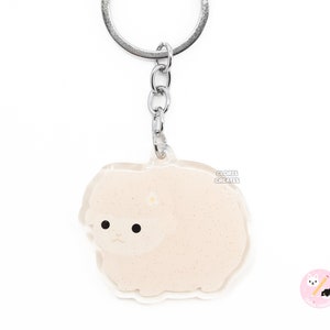 May include: A white fluffy sheep keychain with a silver key ring. The sheep is made of clear acrylic with a glittery finish.
