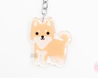 May include: A light orange Shiba Inu dog keychain with a silver key ring. The keychain is made of clear acrylic and has a glitter effect. The dog is standing on all four paws and has a cute expression on its face. The keychain is a great gift for dog lovers.