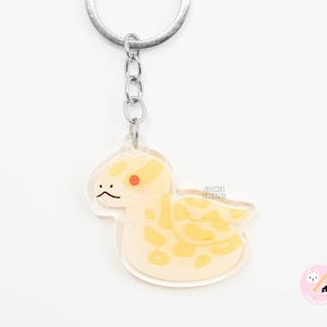 May include: A yellow and white snake keyring with a red eye. The keyring is made of clear acrylic and has a silver metal chain.