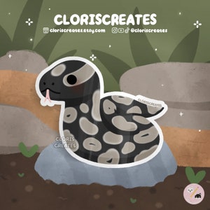 May include: A black and white cartoon snake with a pink tongue curled up on a gray rock. The snake has a cute, cartoonish face with a pink blush. The background is a green and brown forest scene.
