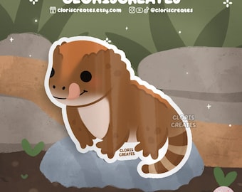 May include: A cartoon illustration of a brown and orange lizard with a long tail and a tongue sticking out. The lizard is sitting on a gray rock with a white outline.
