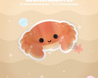 May include: A cute cartoon crab sticker with a smiling face. The crab is orange and has a white outline. The sticker is on a sandy background with white stars.