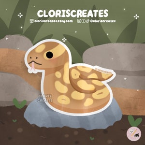 May include: A cartoon illustration of a brown and yellow snake with a pink tongue curled up on a grey rock. The snake has a cute, cartoonish face with large eyes. The background is a green and brown forest.