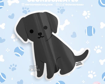 May include: A black Labrador Retriever puppy sticker with a white outline. The puppy is sitting with its ears perked up and its tail curled around its legs. The sticker has a white background with a blue and white pattern.
