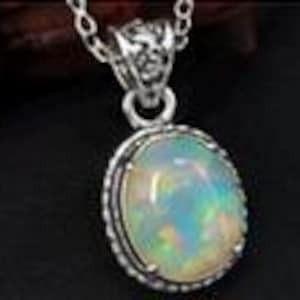 May include: An oval-shaped cabochon opal pendant set in a decorative silver frame with a rope-like border. The pendant hangs from a delicate silver chain, showcasing the iridescent play of color within the milky white gemstone surface.